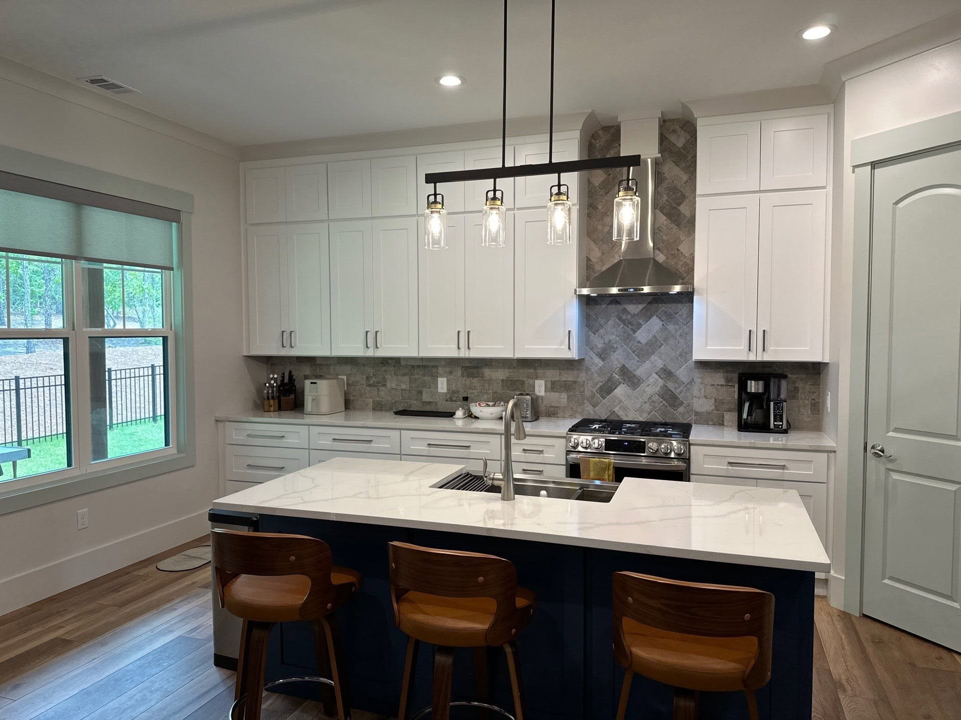 Custom kitchen with full-height cabinetry, herringbone tile, stone counters, and a contrasting island