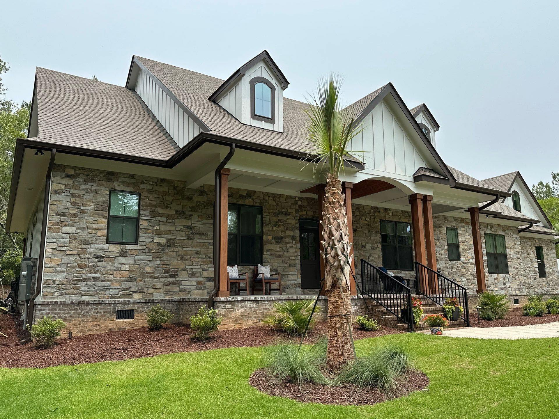 Completed natural-stone custom home with board-and-batten gables, timber porch columns, and detailed rooflines