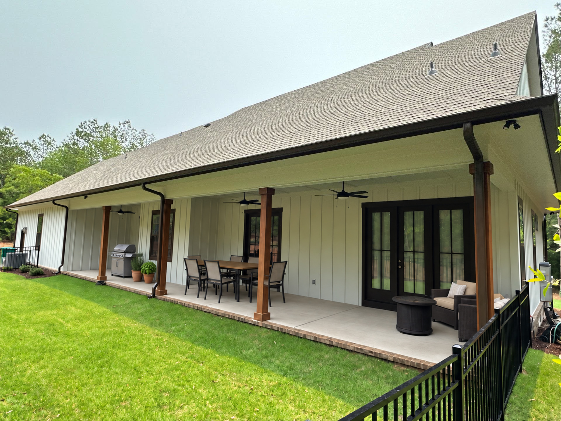 Rear elevation of completed custom home with deep covered porch, timber columns, board-and-batten siding, and outdoor ceiling fans