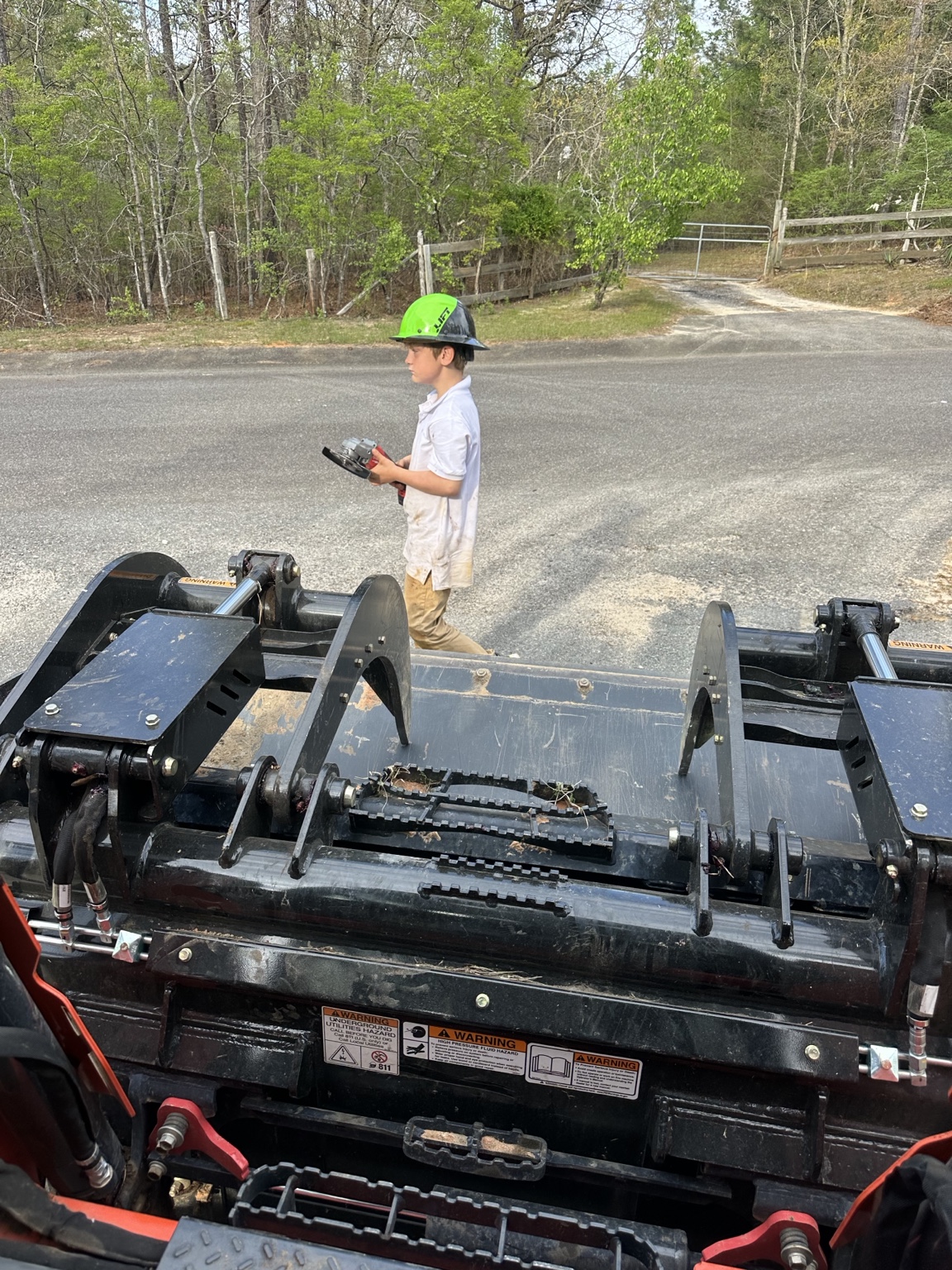 Brycen wearing a hard hat and carrying a handheld tool while helping his dad on a weekend project