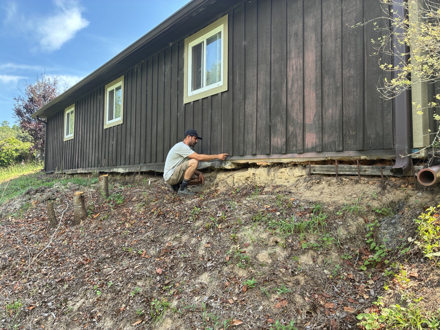 Chase inspecting erosion damage and an exposed lower wall along the side of a stable