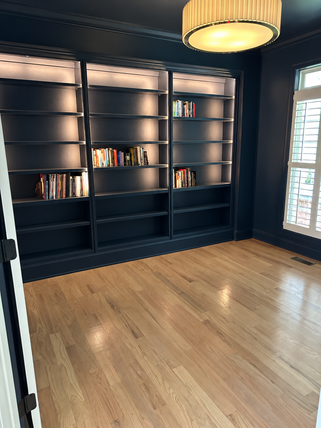 Dark blue library with floor-to-ceiling custom bookcases and integrated lighting