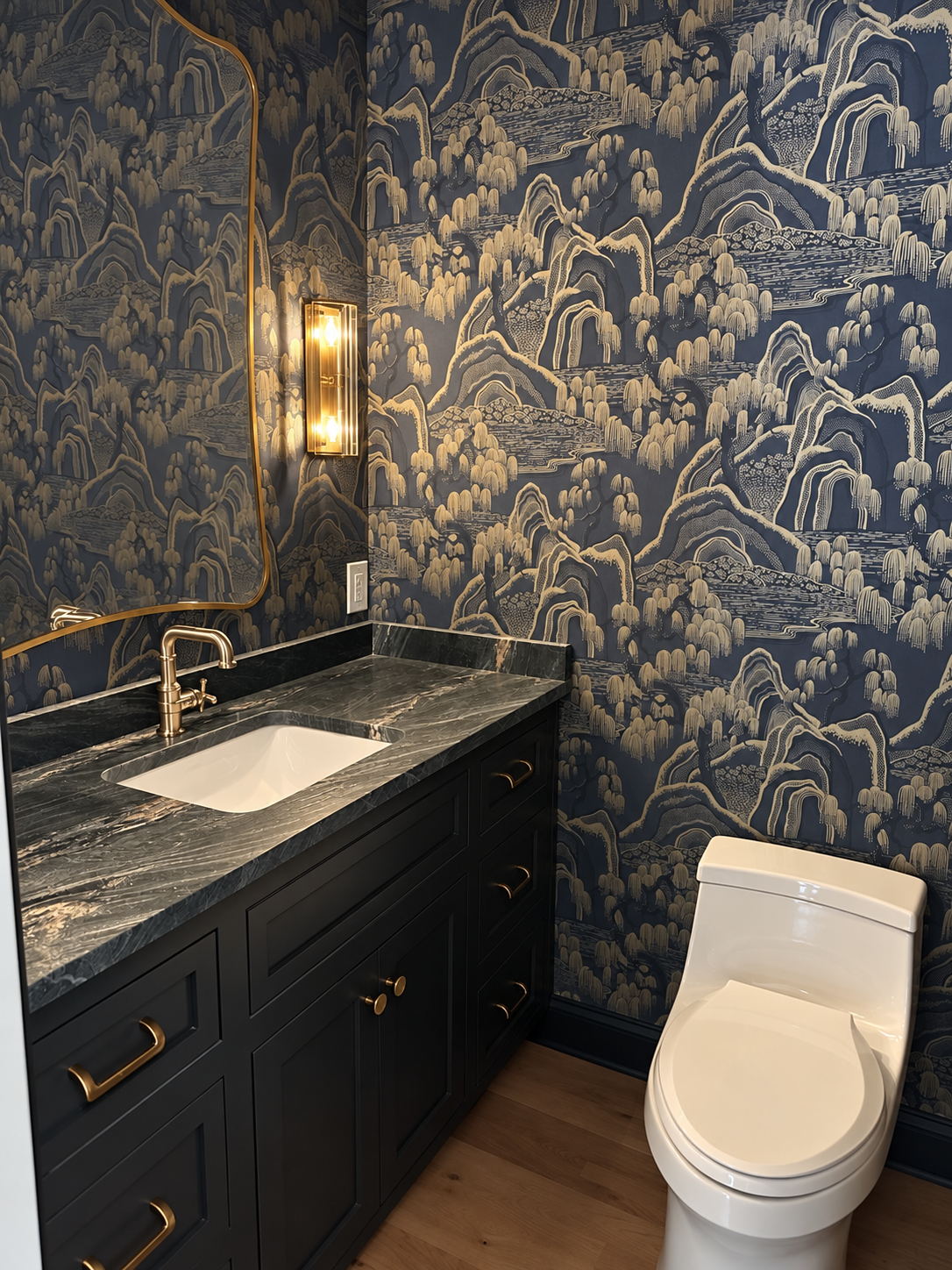 Moody powder room with landscape wallpaper, black vanity, veined stone, and brass fixtures