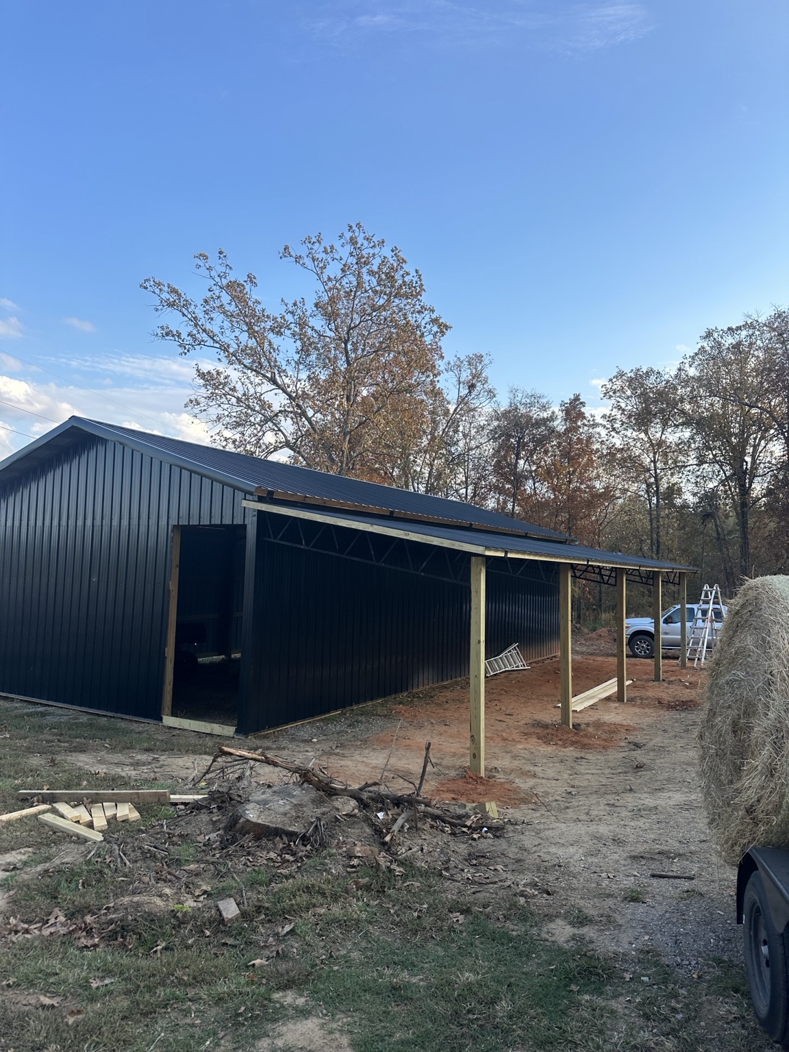 Black metal equestrian barn with a deep shed roof extension under construction