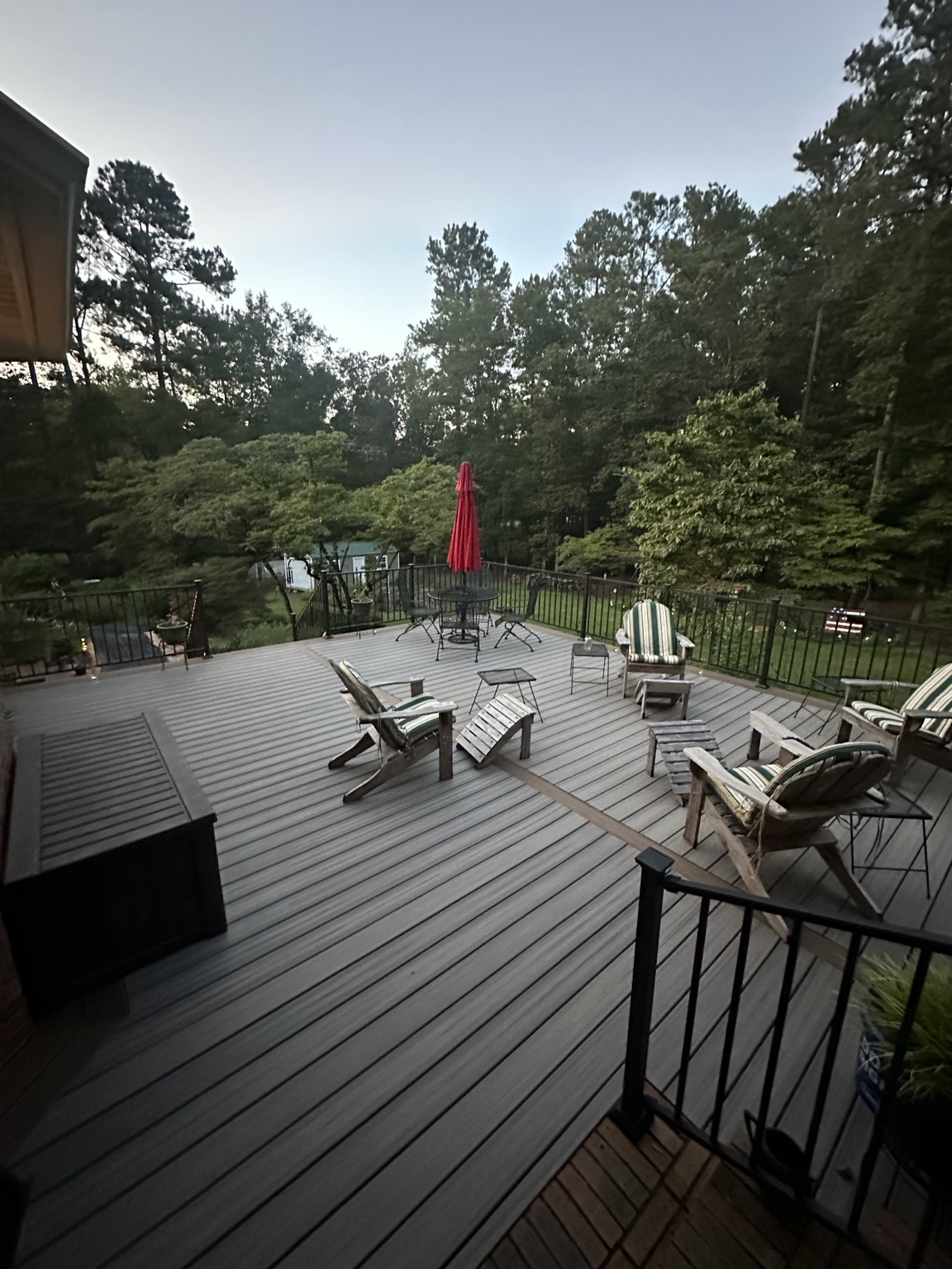 Large finished composite deck with black metal railing arranged for outdoor entertaining in a wooded setting