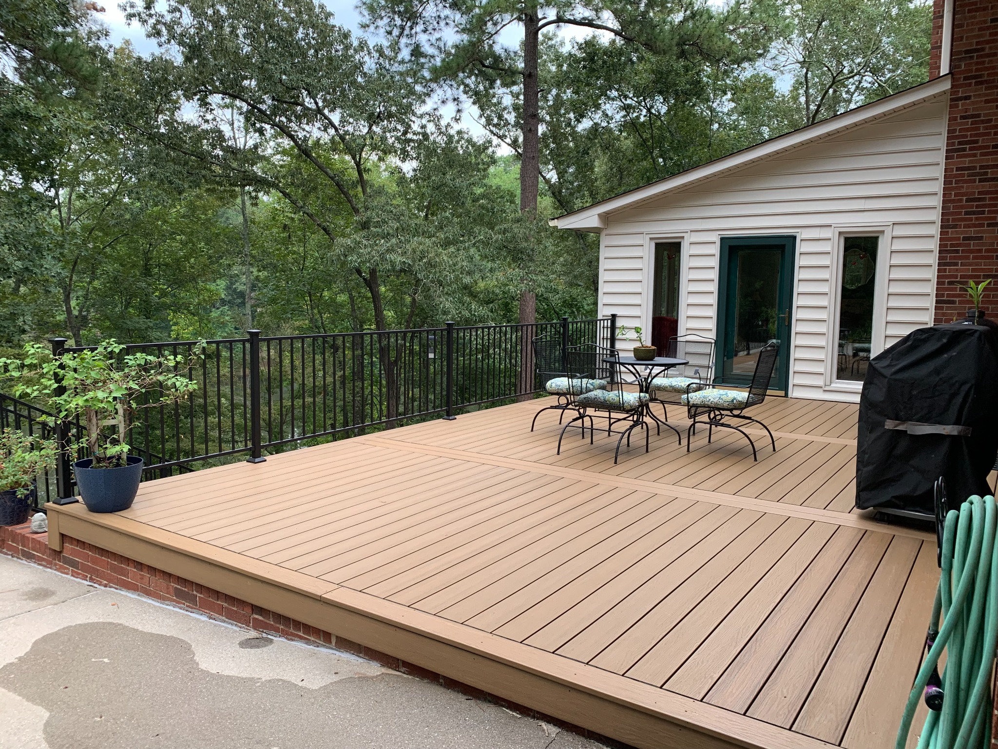 Large composite deck with black metal railing overlooking a wooded yard