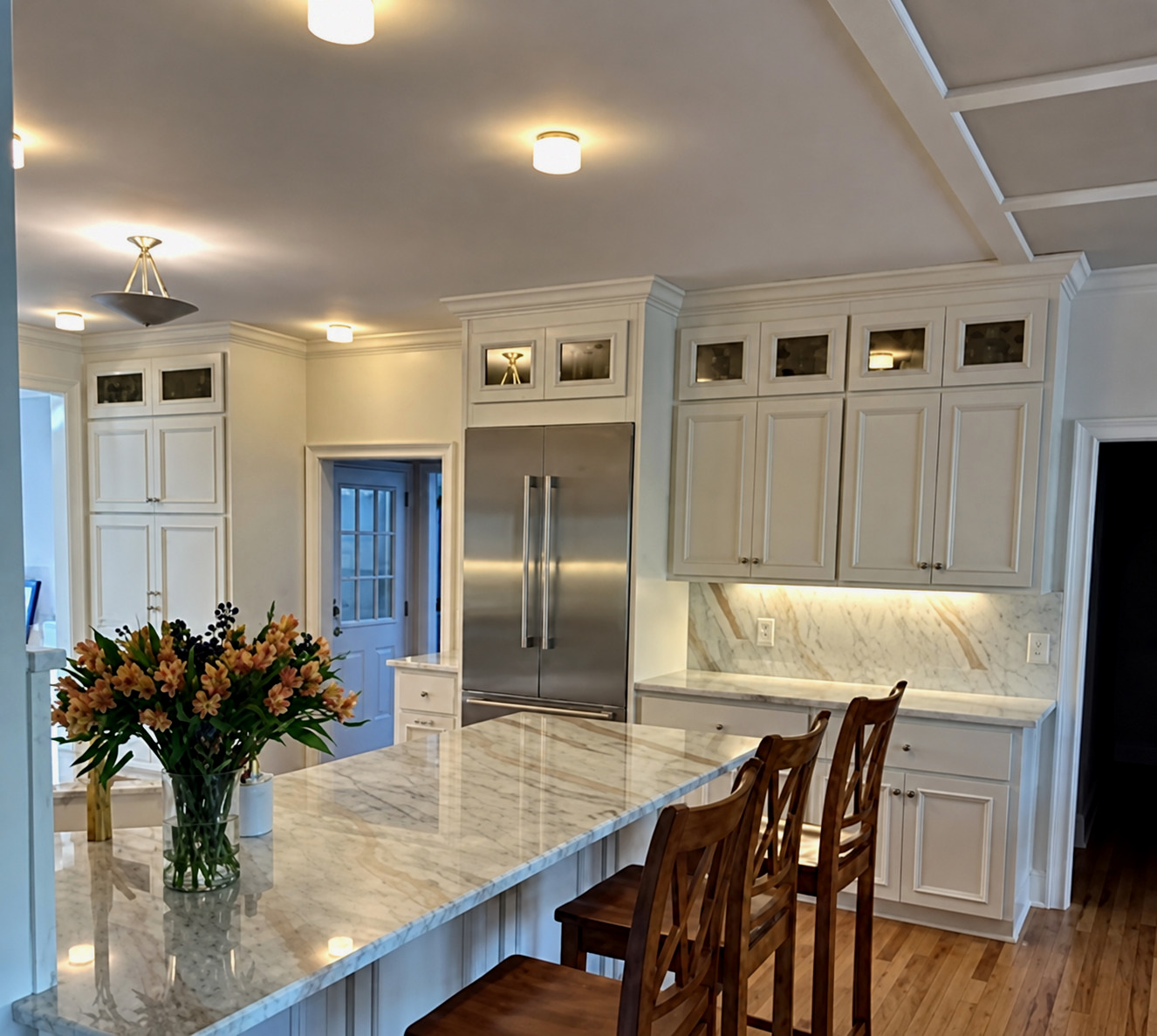 Kitchen island and cabinetry opening into a living room with a coffered ceiling