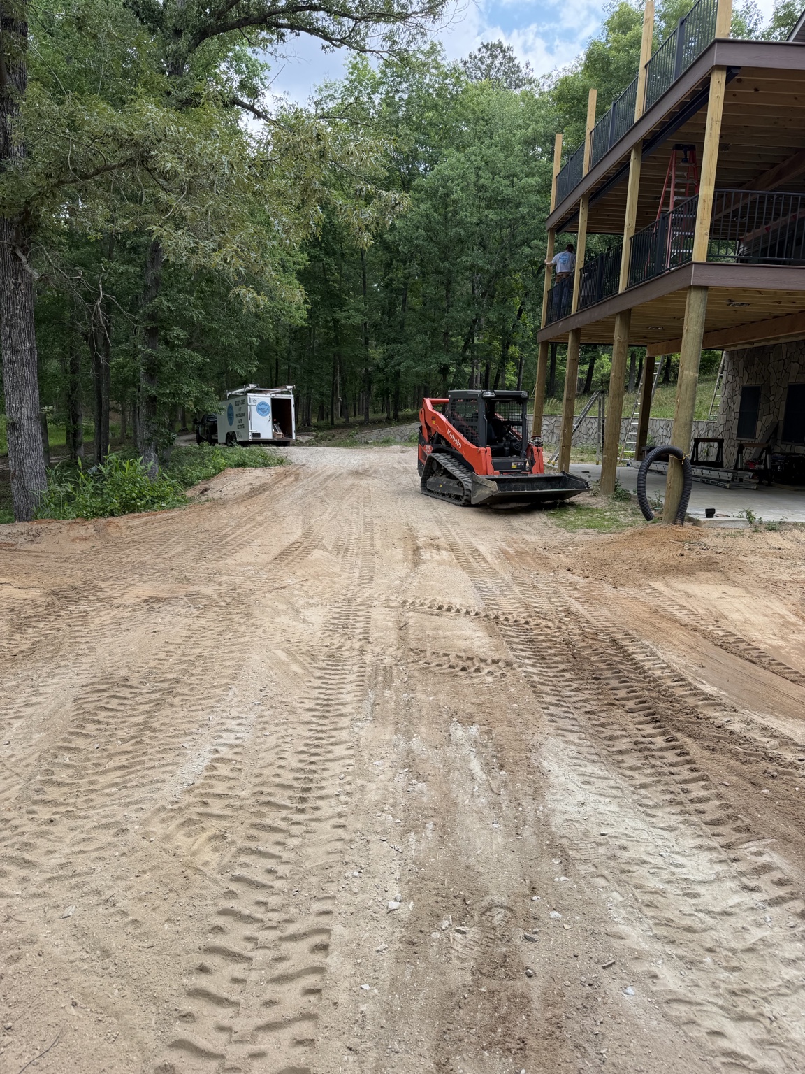 Large two-story deck under construction on a wooded property with black metal railings and heavy timber posts